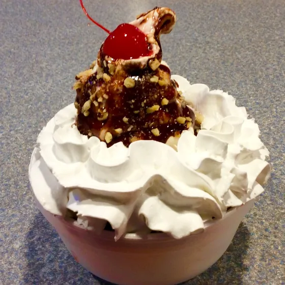 A dessert egg roll served à la mode under whipped cream and a cherry